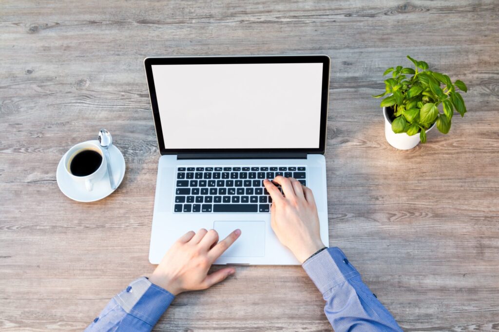 An above view image of a person working on a laptop at a table with a coffee and plant on either side