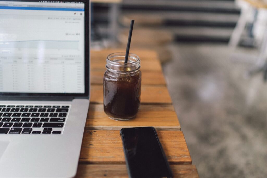 Laptop displaying data analysis on wooden table with iced coffee and smartphone.