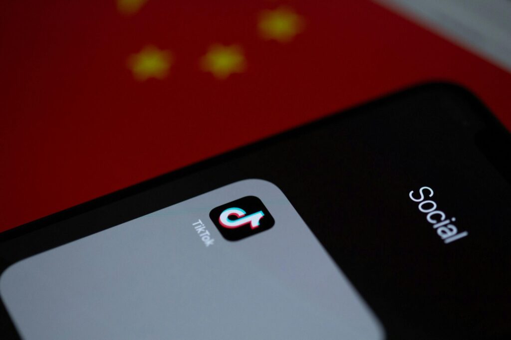 Smartphone displaying the TikTok app, against a backdrop of a red surface with blurred yellow stars, with the word "Social" visible on the phone screen.
